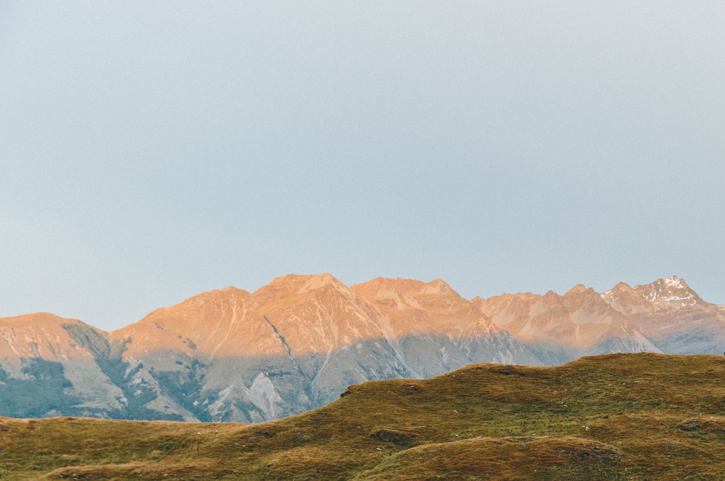 mountain range with grassy hills in the foreground and a clear sky