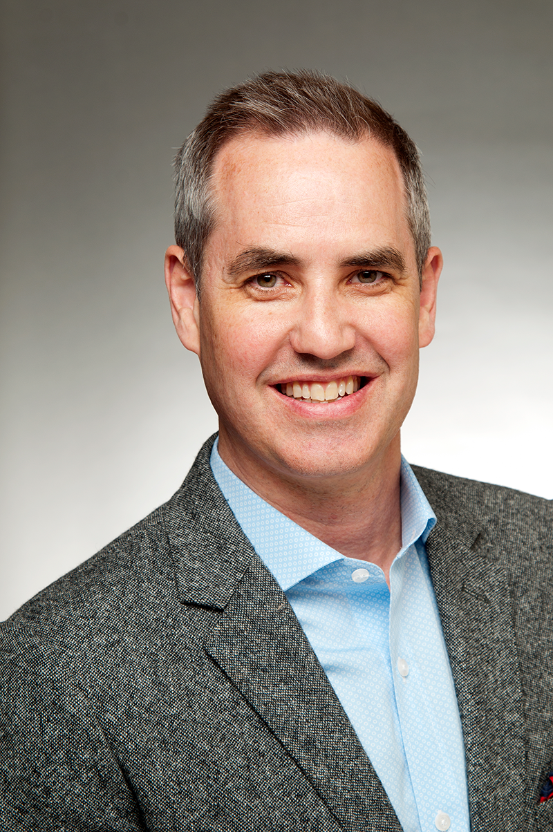 Attorney Darryl Shaper headshot - Smiling man in a gray blazer and light blue shirt, posing against a neutral background.