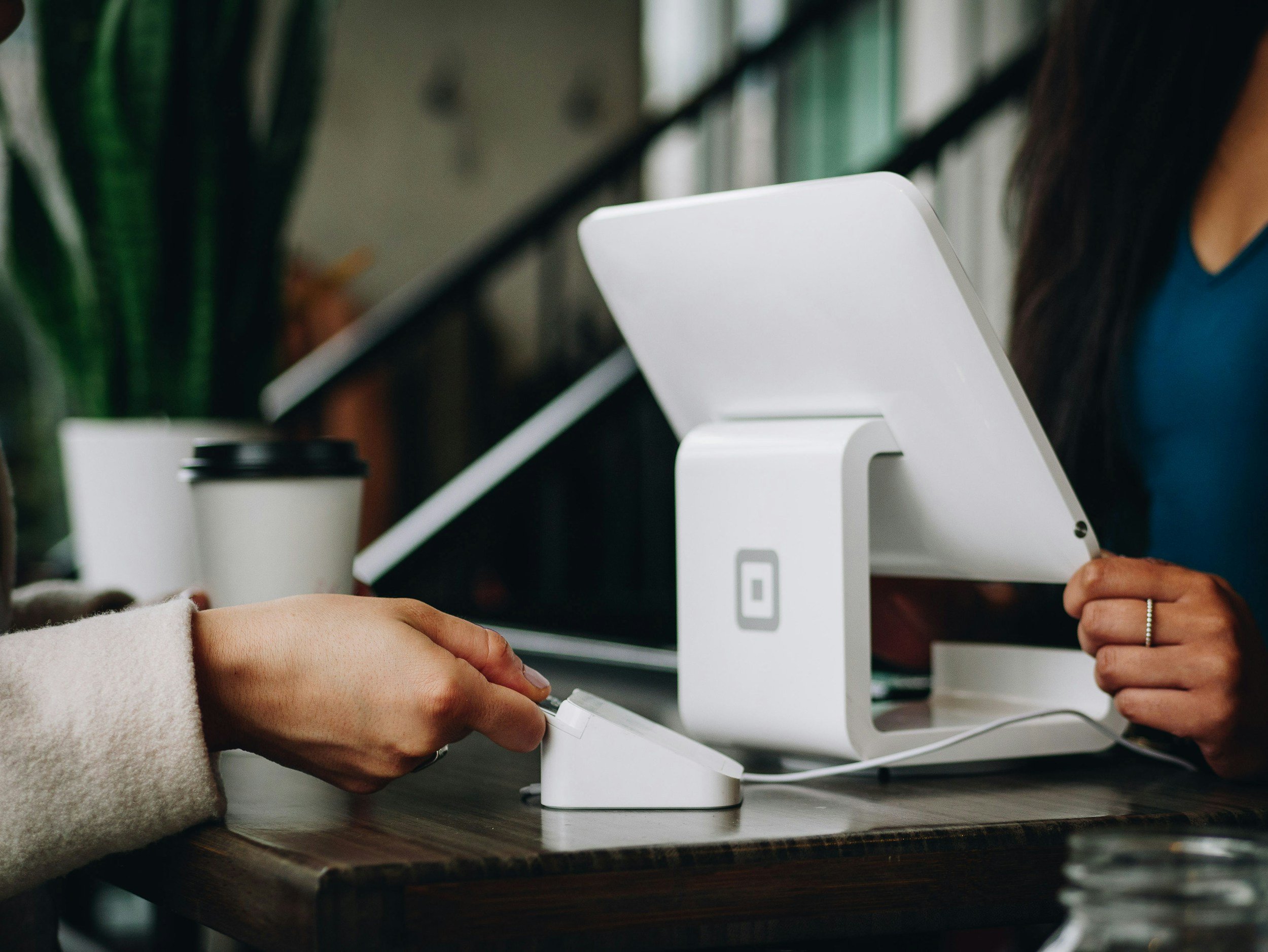 Person at a cash register or point-of-sale system in a coffee shop or cafe, with a coffee cup in the background.