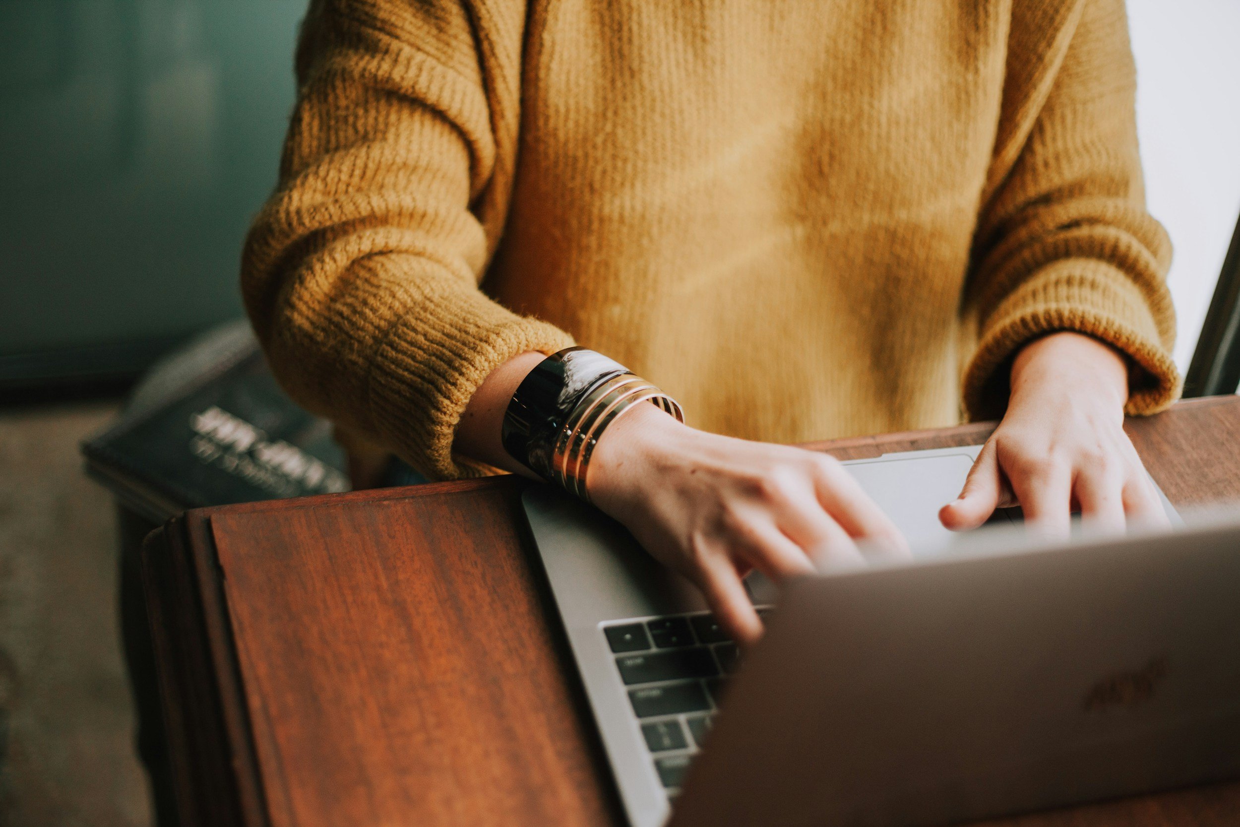 Person wearing a brown sweater using a laptop at a wooden table.